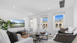 A modern living room with a white sofa, a round coffee table, and a large flat-screen TV mounted on the wall. - Corporate Abode South Yarra by Ready Set Stay (South Yarra)