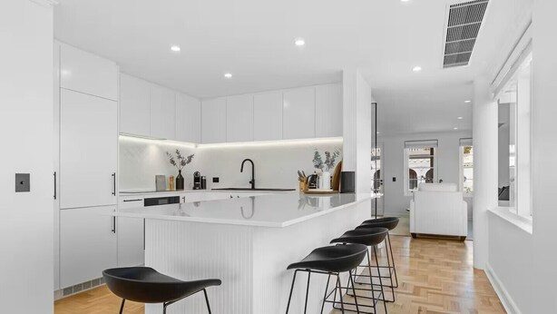A modern kitchen with white cabinetry, a central island with bar stools, and recessed lighting. - Corporate Abode South Yarra by Ready Set Stay (South Yarra)