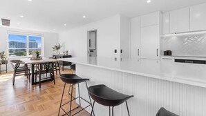 A modern kitchen with white cabinetry, a long countertop, and black bar stools. - Corporate Abode South Yarra by Ready Set Stay (South Yarra)