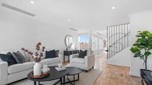 A modern living room with a sofa set, coffee table, and decorative items. A staircase with a metal railing leads to an upper floor. - Corporate Abode South Yarra by Ready Set Stay (South Yarra)
