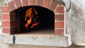 Ein Backofen aus Ziegelsteinen mit Feuer im Inneren und einem Holzstapel darunter.