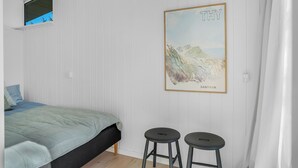 Une chambre à coucher avec un lit, deux tabourets, une fenêtre et un tableau encadré accroché au mur.