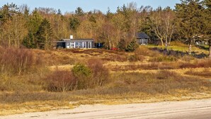 Une propriété située sur la côte, comprenant une grande maison et un bâtiment plus petit, le tout entouré d’une forêt dense et d’une plage de sable.