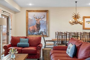 A living room with red leather sofas, a wooden coffee table, a painting of a deer, and a chandelier.