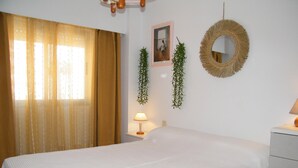 A hotel room with a bed, a bedside lamp, a hanging plant, a framed photo, and a mirror on the wall.