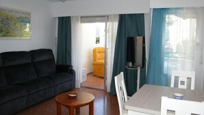 A living room with a sofa, a small table, a TV, and a dining area with a table and chairs.