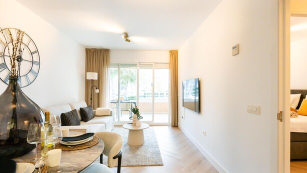 Ein modernes Wohnzimmer mit Essbereich, einer Couch, einem Couchtisch und einem an der Wand montierten Fernseher.
