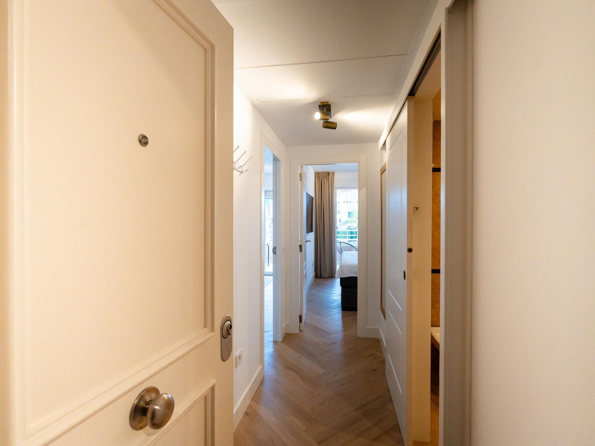 A hallway with a wooden floor, white walls, and a door with a silver handle.