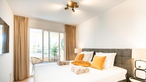 Ein Hotelzimmer mit einem großen Bett, einem Balkon mit Vorhängen, einer modernen Deckenleuchte und Blick ins Freie.