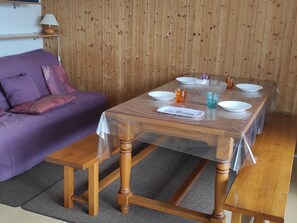 A wooden dining table with a clear plastic cover, surrounded by purple sofas and a wooden wall.