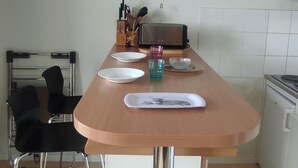 A kitchen with a wooden table, two chairs, a toaster, and a kettle.