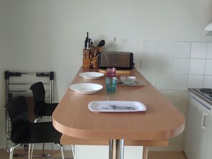 A kitchen with a wooden table, two chairs, a toaster, and a kettle.