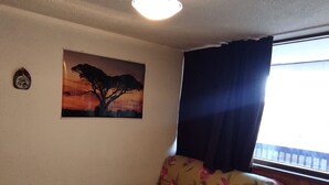 Une pièce avec un canapé, un tableau représentant un arbre et une fenêtre avec des rideaux.