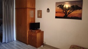 Une pièce avec une armoire en bois, un téléviseur à écran plat posé sur un meuble en bois, un tableau encadré représentant un arbre et un rideau.