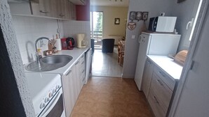 Een compacte keuken met witte apparaten, een spoelbak en een eethoek in de achtergrond.