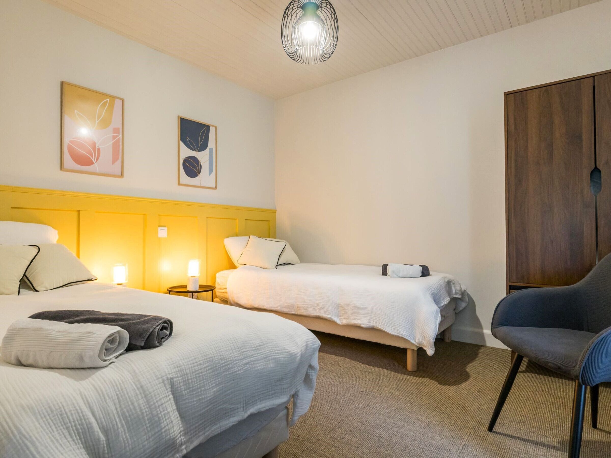 A hotel room with two beds, a chair, and a wardrobe.