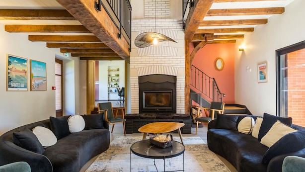 Amplia sala de estar con chimenea, vigas de madera y una escalera que conduce a un nivel superior.