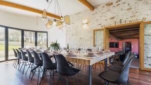 Un comedor con una mesa larga dispuesta para una comida, rodeada de sillas modernas, y una pared de piedra con vigas de madera al fondo.