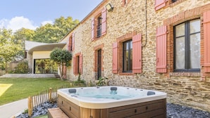 Un edificio de piedra con contraventanas rojas, un jacuzzi y un césped bien cuidado.