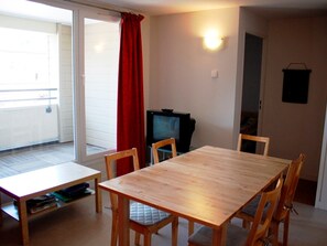A dining area with a wooden table and chairs, a television, and a sliding glass door leading to a balcony. - 3-Bedroom Apartment in Super Besse, Private Parking (Besse-et-Saint-Anastaise-Super Besse)