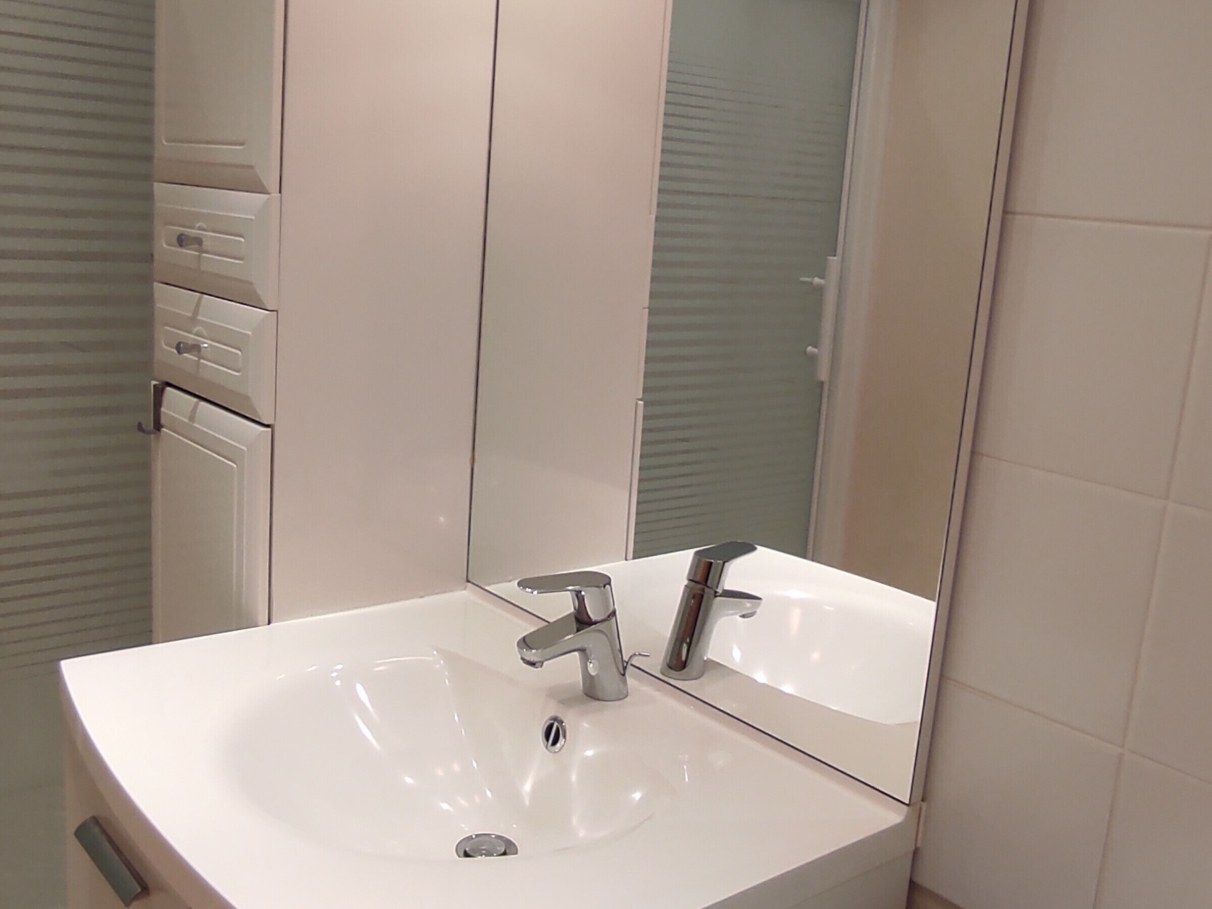 Une salle de bain avec un lavabo blanc, un miroir et une porte dotée d’une poignée.