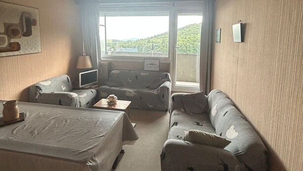 Une pièce confortable avec un lit, un canapé, une petite table et un téléviseur. Il y a une fenêtre qui donne sur un paysage verdoyant.