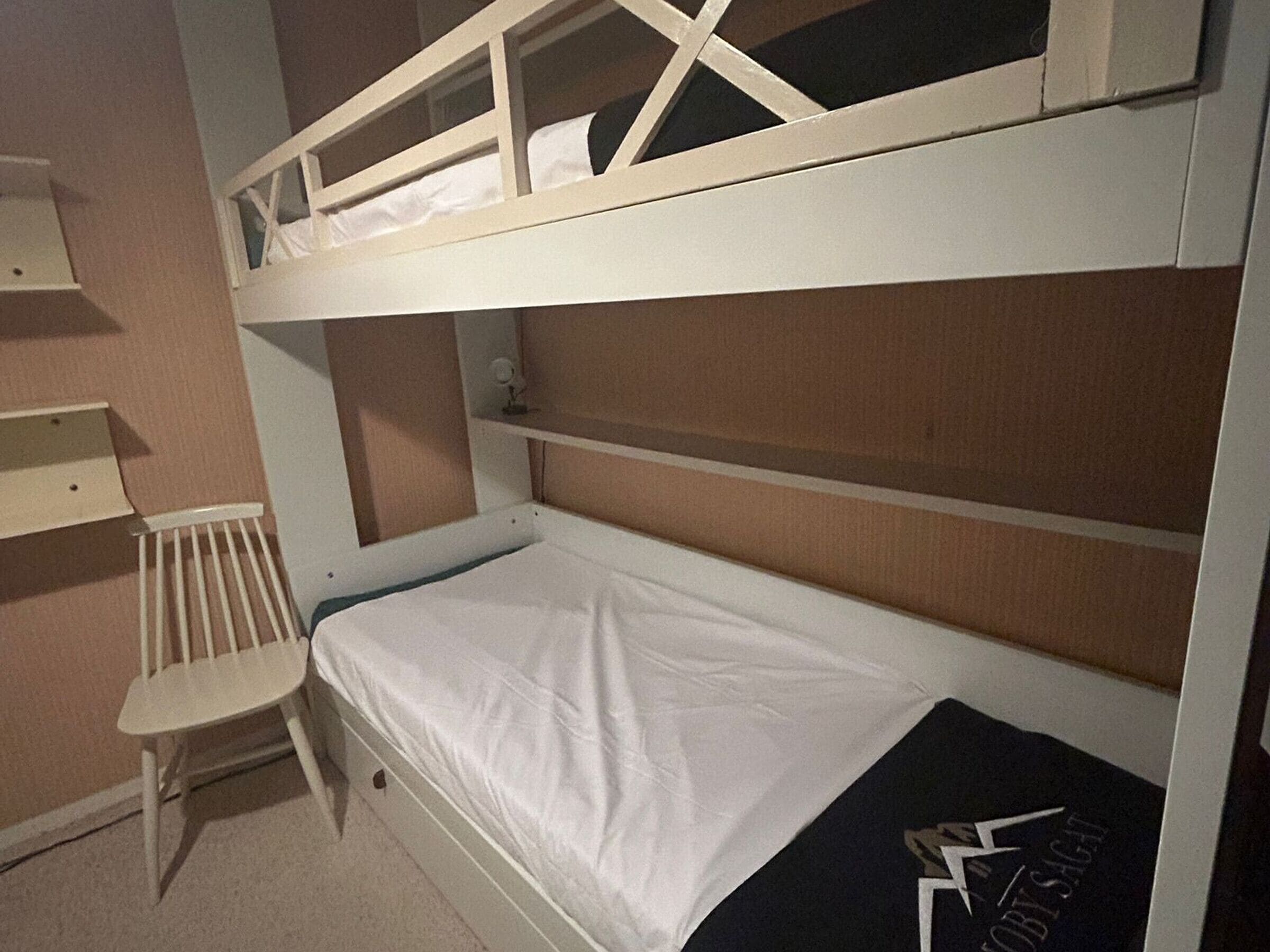 Een stapelbed met een onderbed, een kleine stoel en een plankunit.