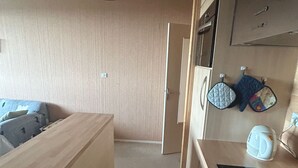 Une cuisine de taille réduite, dotée d’un plan de travail en bois, d’une cuisinière et d’un four à micro-ondes. Une porte donne accès à une autre pièce.