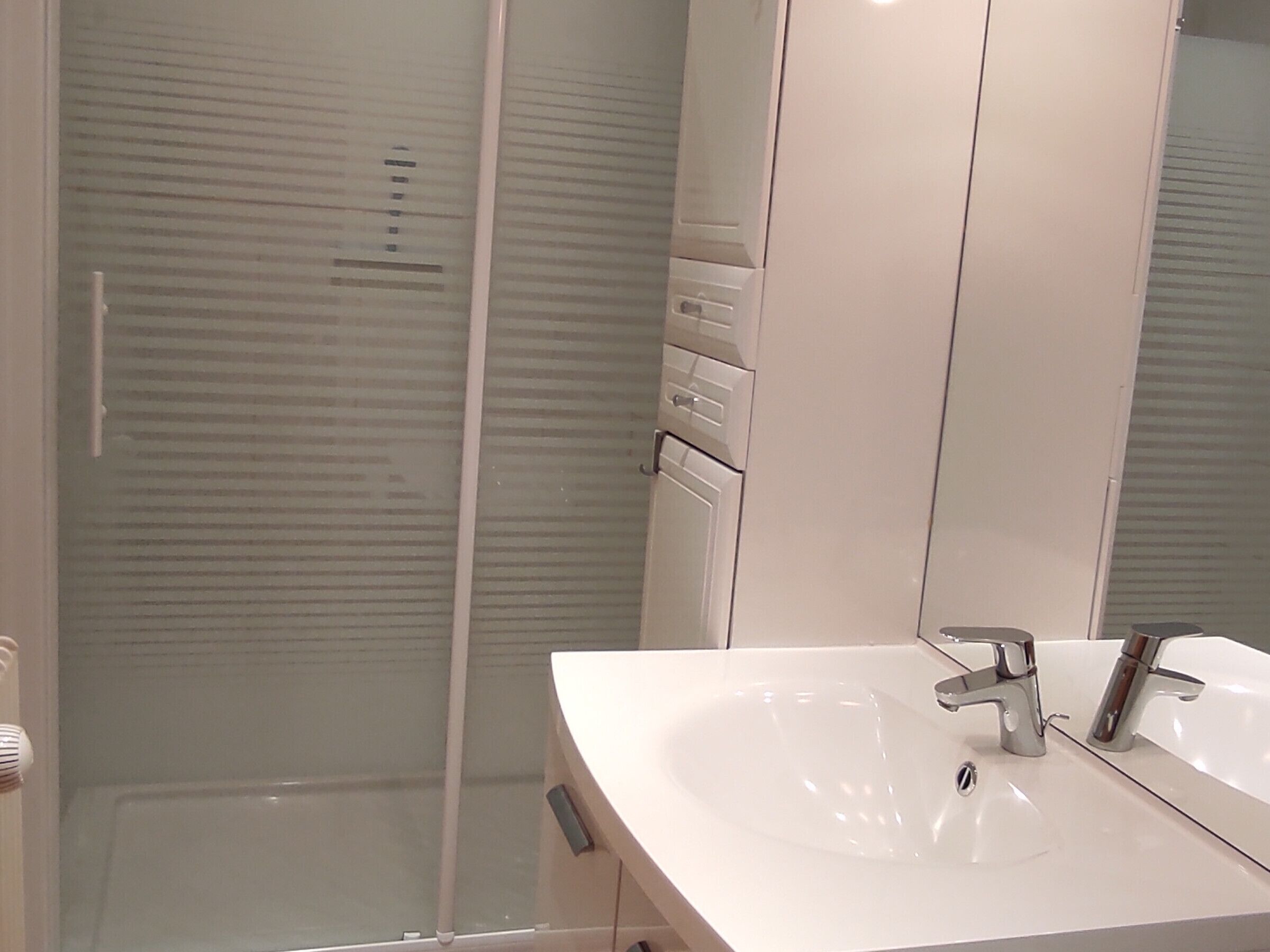 Une salle de bain avec un lavabo blanc, un miroir et une cabine de douche en verre.