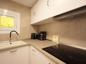 Una cocina con lavamanos, estufa, armarios y cafetera.