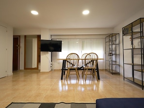 Un coin repas avec une table et des chaises, un téléviseur fixé au mur et une étagère le long du mur.