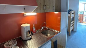 A compact kitchen with a coffee maker, sink, and wooden cabinets. - Ski-in/ski-out studio for 4 people (Besse-et-Saint-Anastaise)