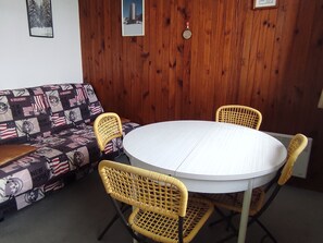 A room with a round white table, four wicker chairs, a patterned sofa, and wooden panel walls.