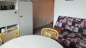 A compact living space with a dining table, two chairs, a sofa with a patterned cover, a microwave, a television, and a refrigerator. - Ski-in/ski-out studio for 4 people (Besse-et-Saint-Anastaise)