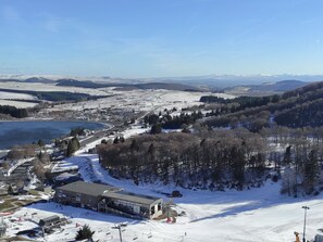 A ski resort with a large building labeled 'TELEPHERIQUE de la Perraux,' a ski lift, and a lake.