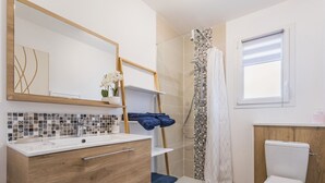 Uma casa de banho moderna com toucador de madeira, chuveiro com porta de vidro e sanita.