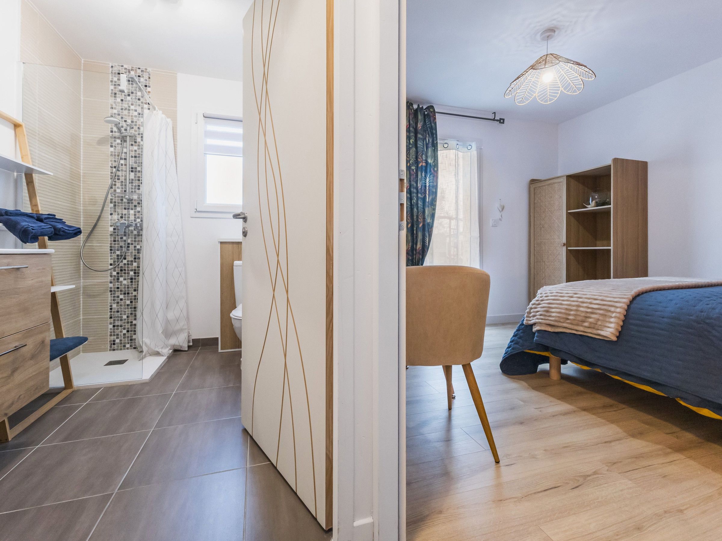 A modern bedroom with a bed, a wardrobe, a chair, and a shower area.