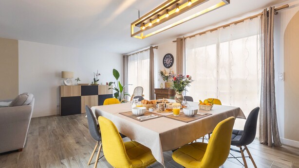 Uma área de refeições com uma mesa posta para o café da manhã, cadeiras amarelas e uma luminária pendente moderna.