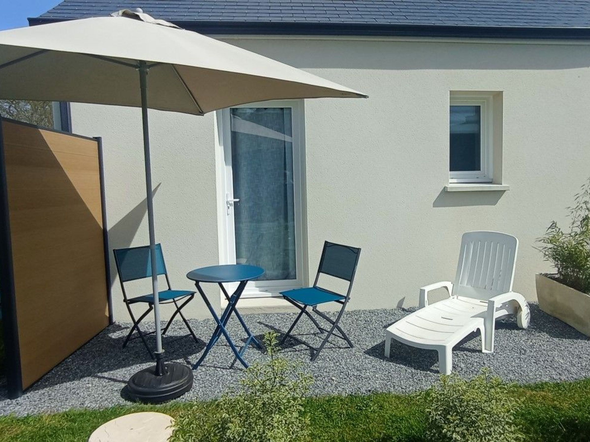 A patio with a table and chairs, a white umbrella, and a white lounge chair.