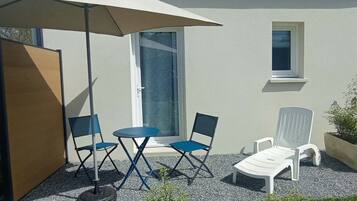 A patio with a table and chairs, a white umbrella, and a white lounge chair.