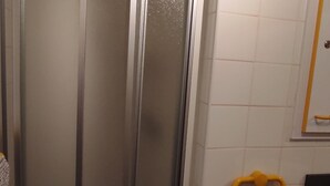 Ein Badezimmer mit Duschkabine aus Glas, weiß gefliesten Wänden und einem gelben Handtuchhalter.