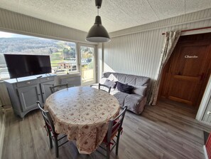 Enjoy a scenic view of the forest from the comfort of this room, featuring a sofa, dining table, and television.