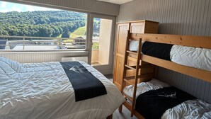 Ein Schlafzimmer mit Etagenbett, einem Einzelbett und einem großen Fenster mit Blick auf eine bewaldete Landschaft.