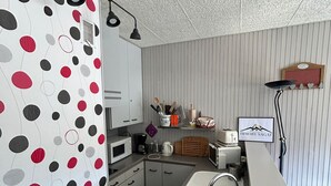 Eine kompakte Küche mit weißen Schränken, einer Mikrowelle, einem Kaffeeautomaten und einem Toaster. Es ist ein Spülbecken mit modernem Wasserhahn zu sehen, und ein kleiner Hocker steht daneben.