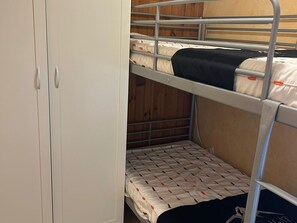 Une chambre avec un lit superposé, une armoire et un lit recouvert d’une couvre-lit à motifs.