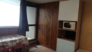 Ein kleines Zimmer mit einer Holzwand, einem Tisch mit einer blumigen Tischdecke, einer Mikrowelle und einem Schrank.