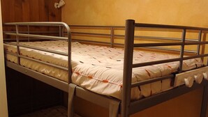 Ein Etagenbett mit Matratze und Kissen, Metallgitter und einer Holzwand.