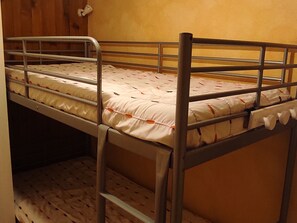 Un lit superposé avec un matelas et des oreillers, des barrières en métal et un mur en bois.