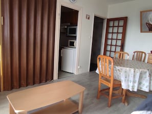 A dining area with a table, chairs, a bench, a microwave, and a refrigerator in the background.