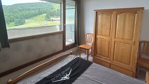 Ein Schlafzimmer mit einem Bett, einem Holzschrank, einem Stuhl und einem Fenster mit Blick auf eine grüne Landschaft.